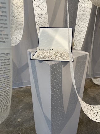 Altered Book on a podium with book pages suspended around it