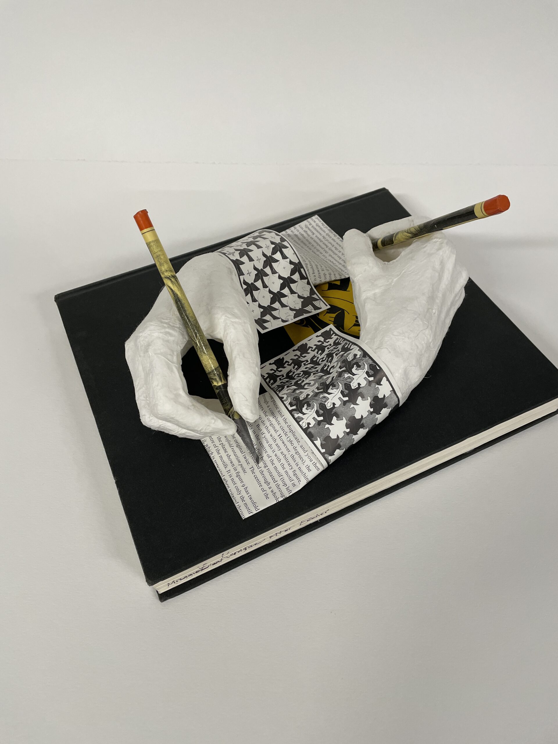 M.C. Escher's famous "drawing hands" have been recreated in 3D by artist Maggie Kerrigan using paper and a book about Escher.