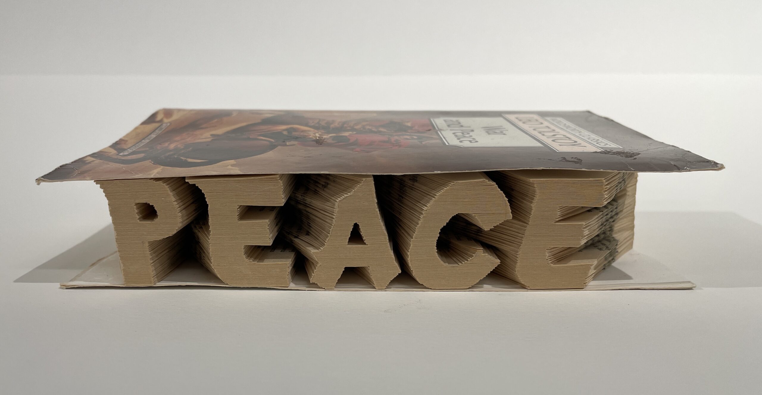 An artwork by Maggie Kerrigan that consists of the word PEACE carved in to the pages of a book--hand done with scissors cutting each page.