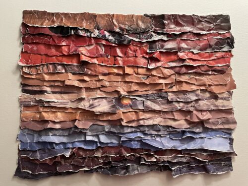 This is an artwork by Maggie Kerrigan that has layers of color that form a sunset. Paper is from a book about shorelines in America.