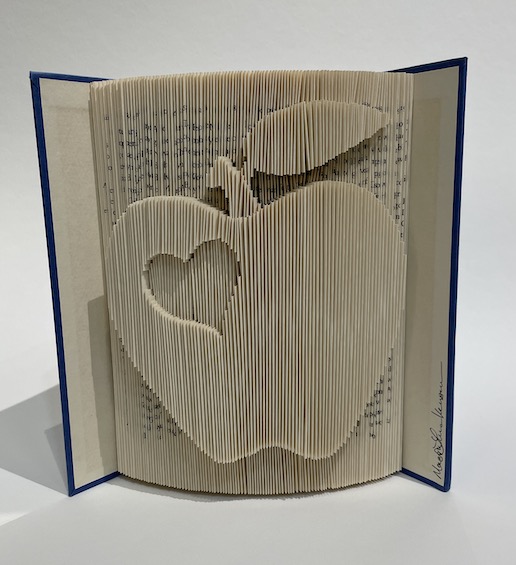An artwork by Maggie Kerrrigan that is a book sculpture in the shape of an apple with a heart in it.