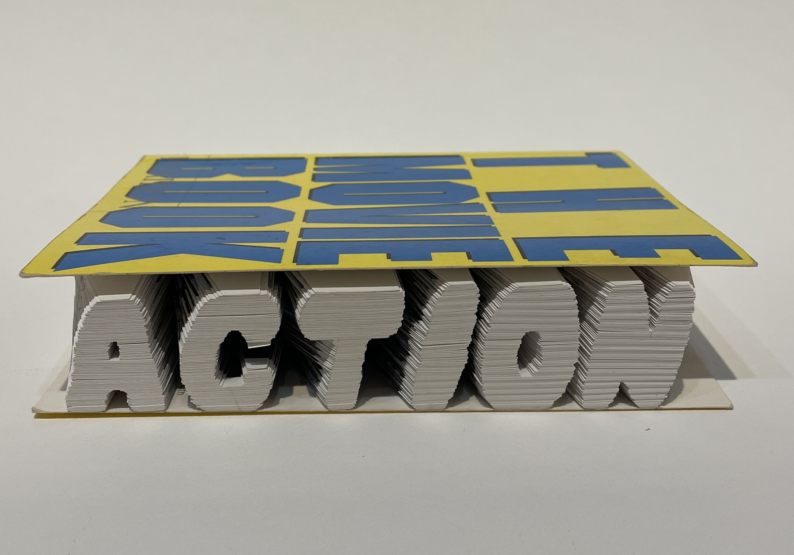 A book that has been carved by hand, by artist Maggie Kerrigan, to show the word "Action." The book cover shows the title, The Movie Book."