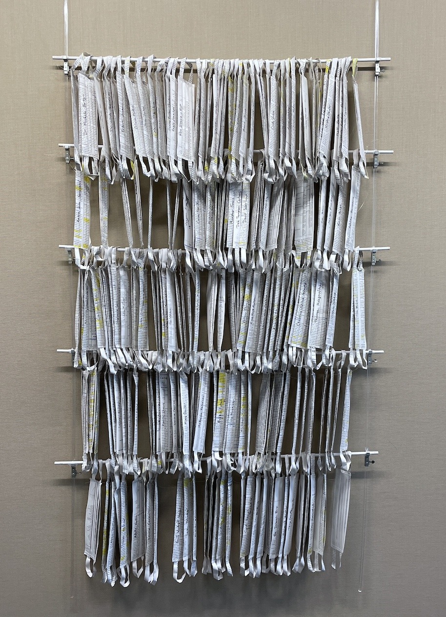 An artwork by Maggie Kerrigan of 250 paper face masks made from a Nursing textbook. Each has a name of a health worker from the early days of the pandemic.