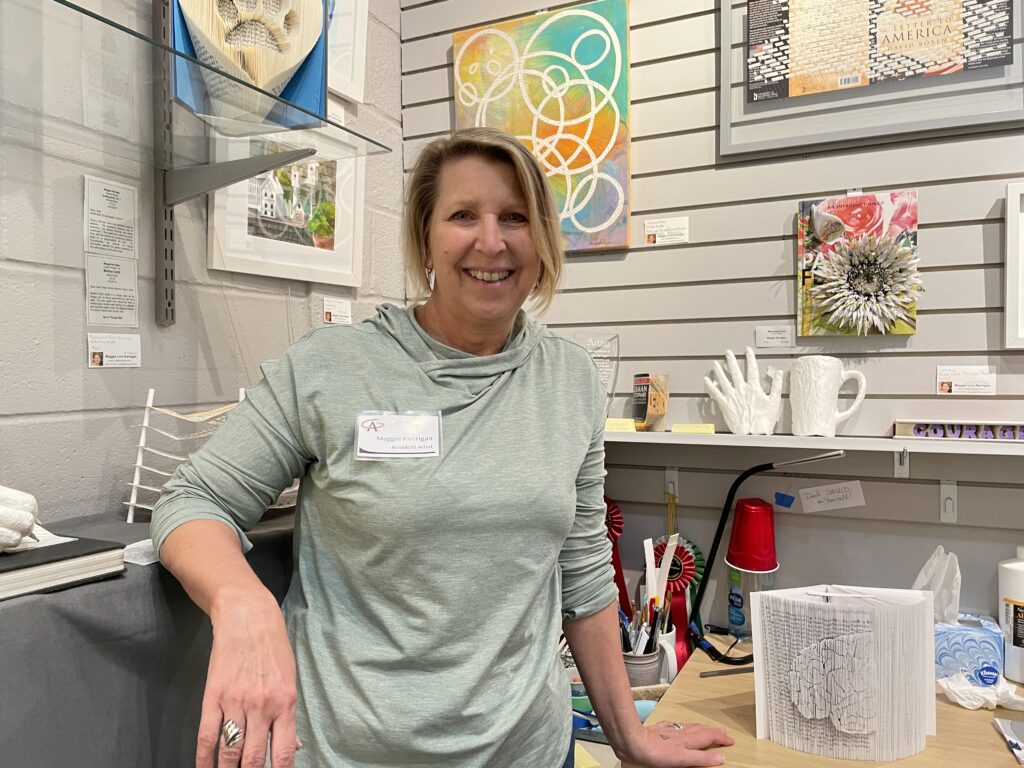 A photo of artist Maggie Kerrigan in her studio surrounded by her altered book art.