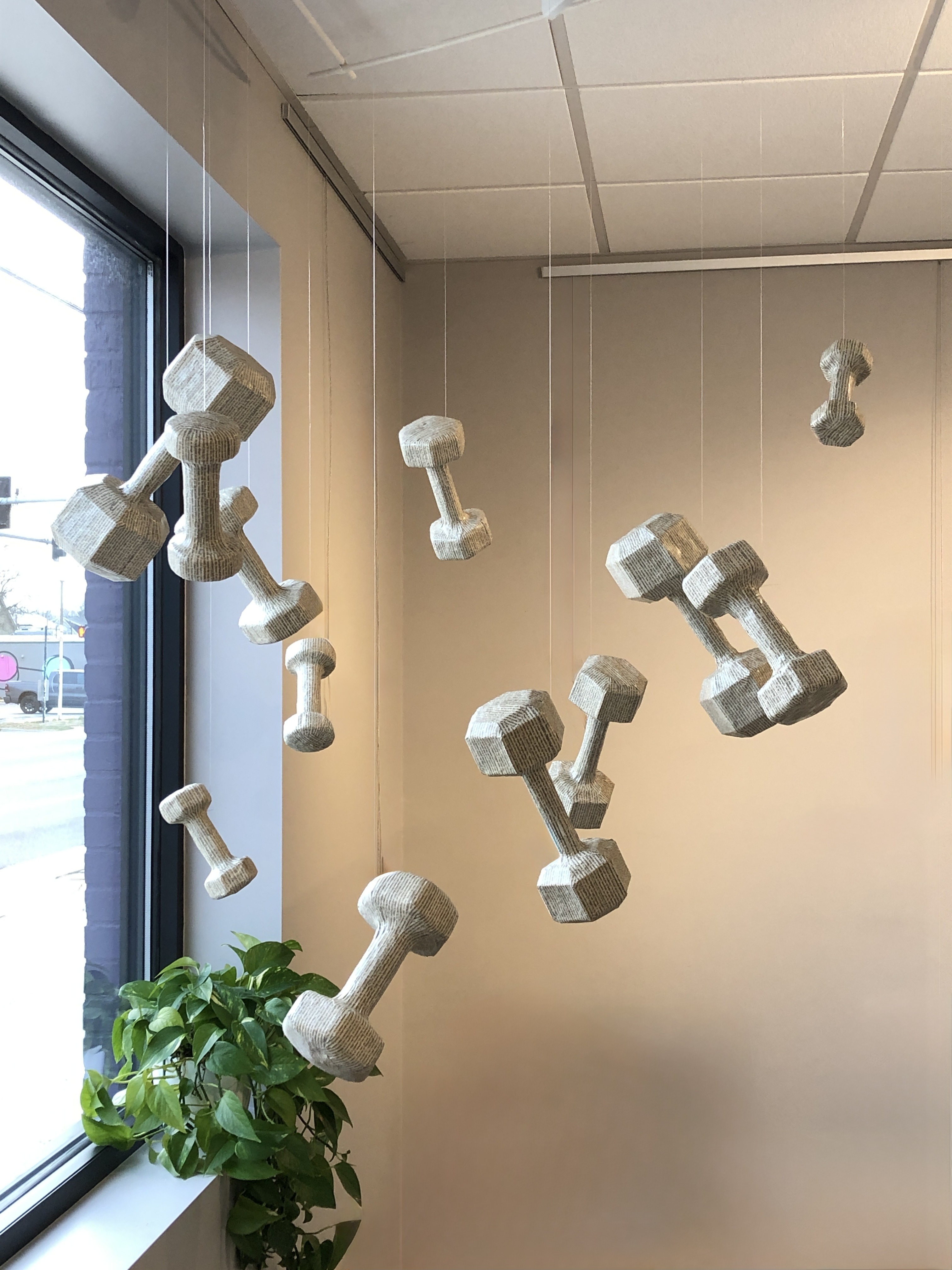 An artwork by Maggie Kerrigan--dumbbells of varying sizes that have been cast out of paper and are seemingly floating in the air.