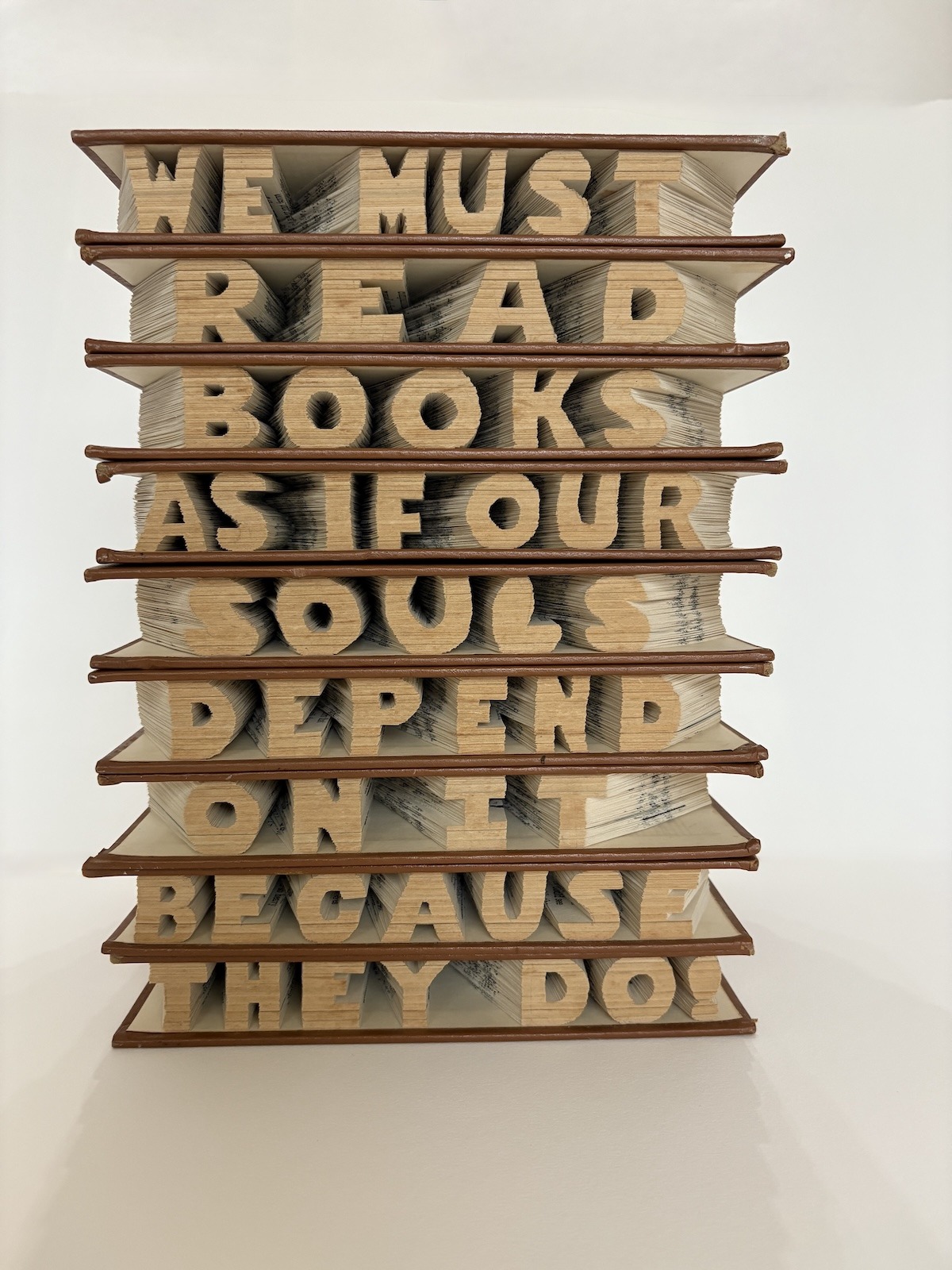 This altered book artwork is stack of 9 books hand-carved by Virginia Beach artist, Maggie Kerrigan, and reads as the sentence "We must read as if our souls depend on it, because they do!"